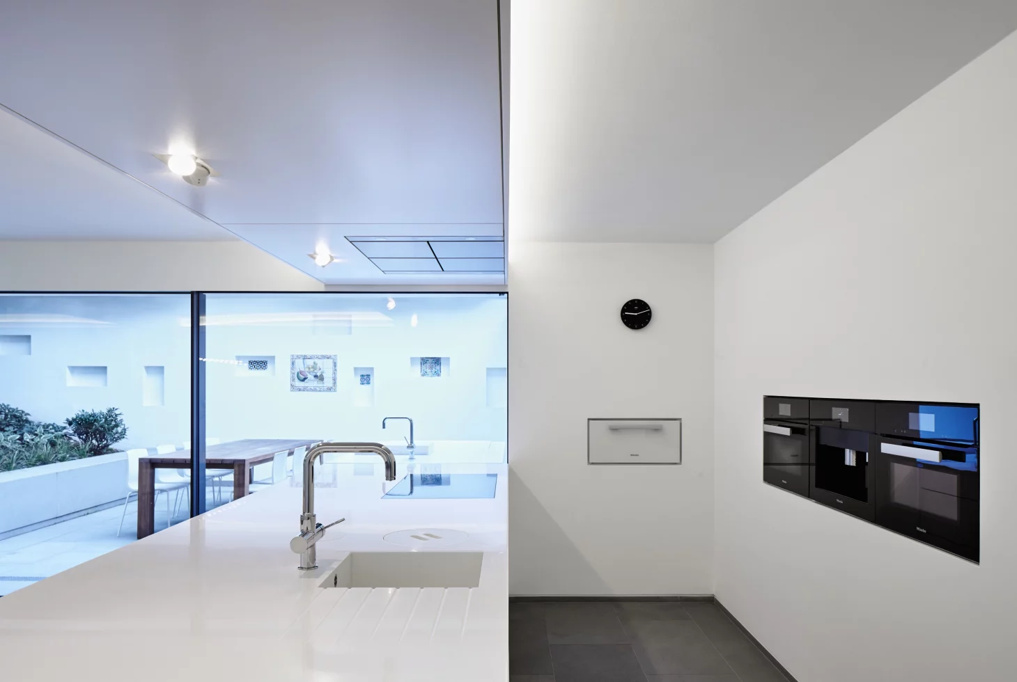 Minimalistische weisse Küche mit weissem Küchenblock und in die Wand eingelassenen Geräten