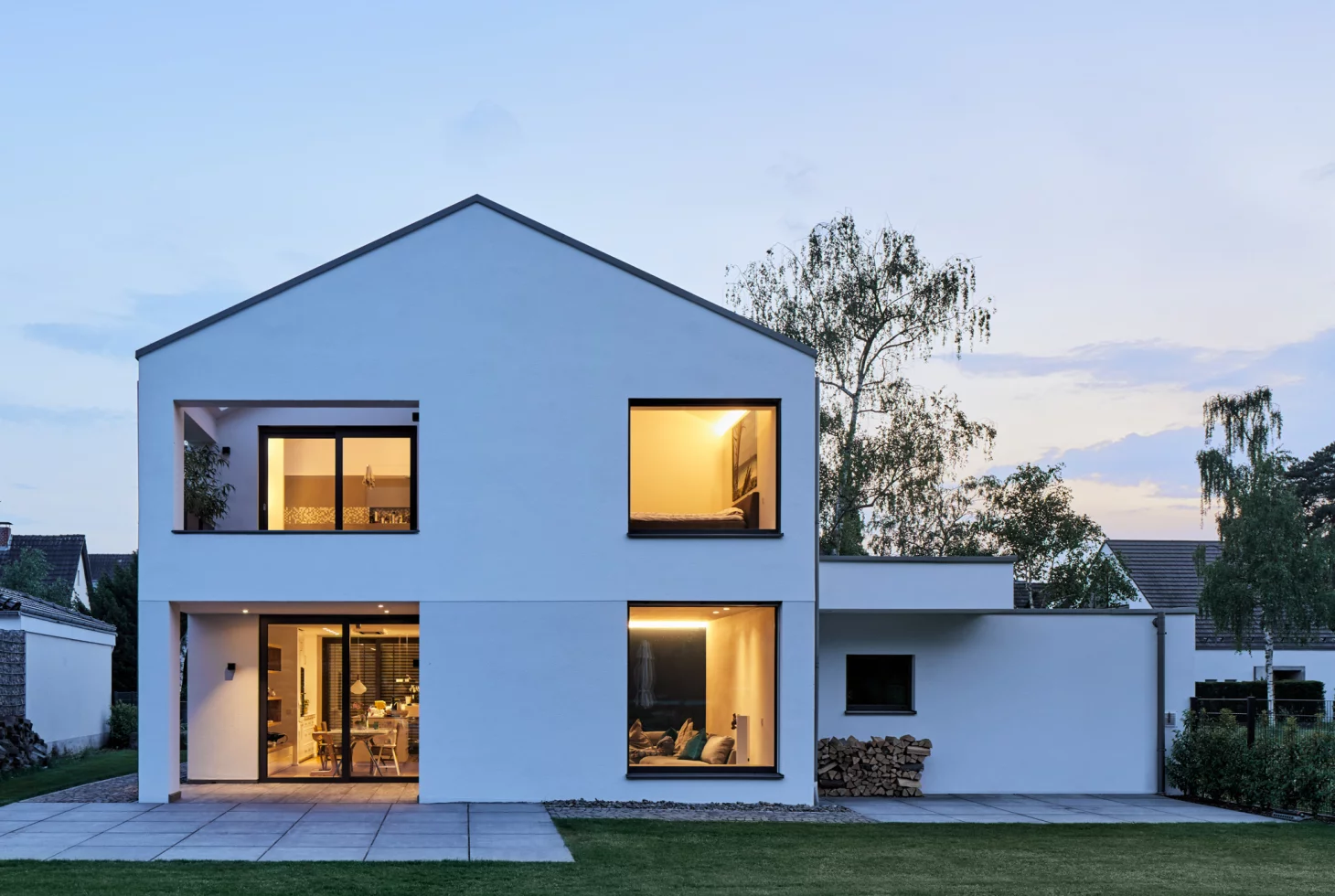 Ansicht der Giebelseite eines minimalistischen, weiss verputzten Einfamilienhauses mit markanten Öffnungen
