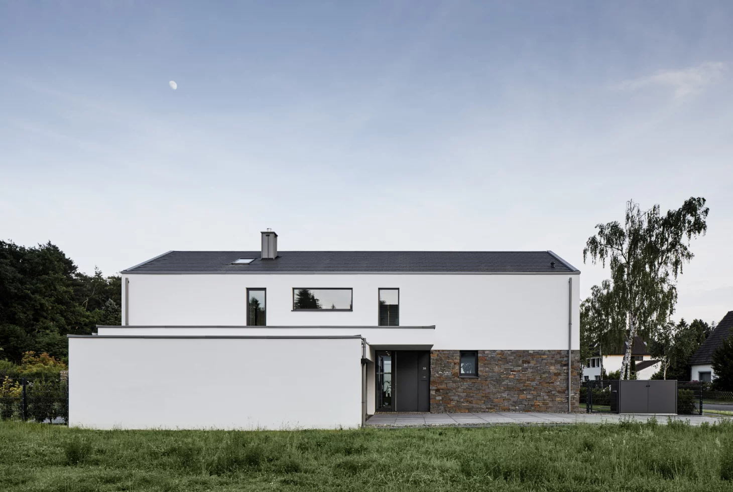 Traufseite eines minimalistischen, weiss verputzten Einfamilienhauses mit Steinsockel