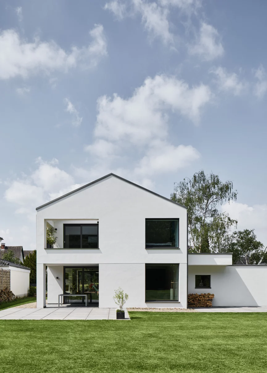Ansicht der Giebelseite eines minimalistischen, weiss verputzten Einfamilienhauses mit markanten Öffnungen